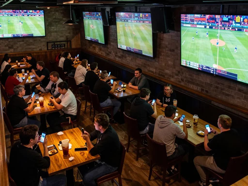Engaged fans placing bets through tg88 while enjoying live sports at a vibrant sports bar.